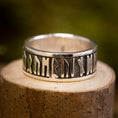 Ladda upp bild i Galleri visare, Sølvring Uovervindelig 925s Sølv, en sølvring med indviklede futhark-runer, hviler på en tekstureret træoverflade, sat mod en sløret grøn baggrund. Ringens indgraveringer, lavet af ægte sølv, består af ældgammelt udseende symboler, der omslutter hele båndet.