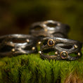 Ladda upp bild i Galleri visare, En trio af mørke, teksturerede ringe fra Eryn Design-kollektionen, med et rustikt, organisk design, hviler oven på en seng af levende grønt mos. To af disse Fingerring - Moria (Simpel) ringe er håndlavede som håndlavede smykker i 925s Sterling Sølv og er prydet med små runde ædelsten sat i gyldne rammer, som tilføjer et elegant touch til den jordiske scene.