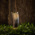Ladda upp bild i Galleri visare, Et poleret, buet Drikkeglas Horn (300 ml), med et skinnende ydre, står oprejst på en overflade omgivet af frisk grønt græs. Baggrunden har en rustik trævæg, der tilføjer en naturlig og jordnær stemning til billedet.