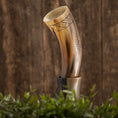 Ladda upp bild i Galleri visare, Drikkehorn Rune, prydet med indviklede mønstre, er placeret på et træstativ mod en rustik træbaggrund. I forgrunden tilføjer grønt græs og planter et naturligt præg til scenen og fremkalder stemningen af vikingemarkeder.