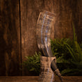 Ladda upp bild i Galleri visare, Drikkehorn Fenrir, lavet af indviklet designet bøffelhorn og poleret til en skinnende finish, vises oprejst ved hjælp af et udsmykket udskåret stativ. Baggrunden har rustikke træpaneler og levende grønne bregner, der giver scenen en naturlig og historisk følelse.