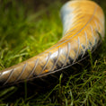 Ladda upp bild i Galleri visare, Et nærbillede af et poleret Drikkehorn Wild, et traditionelt jødisk ceremonielt horn, hvilende på frodigt grønt græs. Hornet fremviser indviklede riller og en gradient fra gule til mørke nuancer, der reflekterer lyset og fremhæver dets detaljerede tekstur. Dens håndværk minder om det, man finder i Vikingemarkeder.