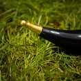 Ladda upp bild i Galleri visare, En poleret Drikkehornulv ligger på grønt græs. Det let buede, vintage sorte og guld horn har en skinnende sort krop og et guld ornamentalt mundstykke. Nærbilledet fremhæver græssets tekstur og hornets håndværk – perfekt til vikingemarkeder.