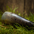 Ladda upp bild i Galleri visare, Drikkehorn Helleristning, prydet med indviklede keltiske udskæringer, ligger på græs mod en sløret træbaggrund, der fremkalder atmosfæren af vikingemarkeder.