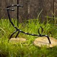 Ladda upp bild i Galleri visare, En Drickshorn Spiral-skulptur i svart metall står på två runda träbaser på gräs, med ett plankstaket i bakgrunden. Figuren, som minner om dekorationer på vikingamarknader, ser ut att vara i en dynamisk, sned pose.
