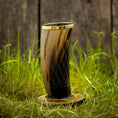 Ladda upp bild i Galleri visare, Et højt, poleret Drikkeglas Horn med mønster (300ml) med en guldkant sidder på et træstativ oven på levende grønt græs, i kontrast til en rustik træbaggrund. Dette udsøgte drikkehorn har et diamantmønster og kan prale af elegante brune og sorte nuancer.