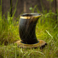 Ladda upp bild i Galleri visare, Drikkeglas Horn med Mønster (100 ml), med en guldkantet kant, står oprejst på en træbund. Hornet har et indviklet mønster på kryds og tværs og vises på en græsklædt udendørs overflade med en sløret baggrund af frodigt grønt og træhegn.