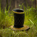 Ladda upp bild i Galleri visare, Et Drikkeglas Horn med Mønster (100 ml), med et indviklet sort design med guldaccenter, er placeret på en træskranke omgivet af levende grønt græs. Baggrunden er let sløret, hvilket gør opmærksom på det unikke glass detaljerede mønster og skinnende finish.