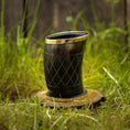 Ladda upp bild i Galleri visare, Et poleret Drikkeglas Horn med Mønster (100ml) med guldkant og indviklede udskårne mønstre er placeret på en træbund, omgivet af grønt græs. Baggrunden viser et rustikt plankeværk.