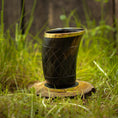 Ladda upp bild i Galleri visare, Et dekorativt Drikkeglas Horn med Mønster (100ml) med guldkant står på en træskive placeret på grønt græs. Skålen har et indviklet udskåret mønster og har en poleret finish, hvilket skaber et rustikt og naturligt udseende. Baggrunden er let sløret og fokuserer opmærksomheden på koppen.