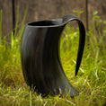 Ladda upp bild i Galleri visare, Et Vikingekrus Nature Horn (600-800ml) med et sort, hornformet design og et buet håndtag sidder på grønt græs, sat mod en sløret træbaggrund. Dette krus efterligner et traditionelt drikkehorn, perfekt til dem, der værdsætter historien og æstetikken ved store drikkekrus.
