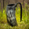 Ladda upp bild i Galleri visare, Et Vikingekrus Nature Horn (600-800ml) med et håndtag, prydet i et marmoreret sort og gråt mønster, står oprejst på græsklædt terræn med en træbaggrund. Dette stykke legemliggør essensen af vikingekrus, der forener tradition og håndværk.