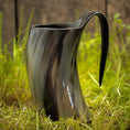 Ladda upp bild i Galleri visare, Et poleret, buet Vikingekrus Nature Horn (600-800ml) med et håndtag, stående på græsklædt jord med en sløret træbaggrund. Dette sorte drikkehorn har en blank finish og naturlige teksturerede mønstre, hvilket giver et unikt og rustikt udseende.