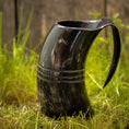 Ladda upp bild i Galleri visare, Et poleret sort Vikingekrus Helleristning Horn (600-800ml) med to dekorative bånd vises oprejst på græs med en træbaggrund. Håndlavede hornkrus har et håndtag, der giver den et kruslignende udseende.