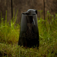 Ladda upp bild i Galleri visare, Et sort keramik Vikingekrus Thors Hammer Horn (600-800ml) med et håndtag og en tud, med et stiliseret Thors hammerdesign ætset på forsiden, er placeret på en plet af grønt græs mod en træbaggrund. Denne vikingekrus udstråler robust charme.