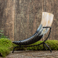 Ladda upp bild i Galleri visare, Drickshorn-hjorten med ett polerat horn i gradient från svart vid basen till beige i spetsen är elegant monterad på ett svart smidesjärnsstativ och står på en mossbelagd träyta mot en rustik träbakgrund – perfekt för vikingamarknader.