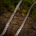 Ladda upp bild i Galleri visare, Nærbillede af to Halskæde Panzering 5,5 mm 925s Sølv-kæder lagt parallelt på et stykke struktureret, barkbeklædt træ. Grønt mos omgiver halskæden og tilføjer et naturligt element til scenen. Kæderne har et zigzag-mønster og et geometrisk, sammenhængende design i kontrast til den organiske baggrund.