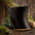 Ladda upp bild i Galleri visare, Dricksglas Horn Plain (500 ml) står elegant upprätt på en texturerad träyta och visar sitt släta, böjda svarta buffelhorn med en solbrun bas. Bakgrunden har träbitar och fläckar av grön mossa som förstärker scenens rustika, naturliga känsla.