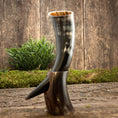 Ladda upp bild i Galleri visare, Et poleret Drikkehorn Yggdrasil U. Mønster står på en træoverflade med en lille grøn kulisse. Hornet har en naturlig buet form og holdes oprejst af et træstativ. Scenen, der minder om Yggdrasils rødder, fremkalder en rustik, historisk stemning svarende til, hvad du ville finde på et vikingemarked.