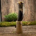 Ladda upp bild i Galleri visare, En poleret Drikkehorn Templar med gyldne graveringer hviler i et indviklet formet hornstativ. Opsætningen er placeret på en rustik træflade med en plet grønt og en trævæg i baggrunden, hvilket skaber en middelalderlig æstetik, der minder om vikingemarkeder.