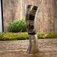 Ladda upp bild i Galleri visare, Drikkehorn Yggdrasil med Mønster, en poleret hornkar, der minder om traditionelle drikkehorn, hviler på en træoverflade med mos og grønt i baggrunden. Denne udsøgt udformede tankard byder på indviklede graveringer og et detaljeret design af et træ med indvævede grene og rødder - perfekt til naturentusiaster eller vikingemarkeder aficionados.
