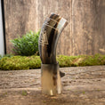 Ladda upp bild i Galleri visare, En Drikkehorn Valknut med polerede finish og indgraverede geometriske designs vises opretstående på en træbund. Baggrunden har en rustik trævæg og grønt mos, der forstærker den autentiske vikingestemning.