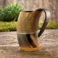 Ladda upp bild i Galleri visare, Et rustikt, håndlavet Vikingekrus Bark Horn (600-800ml) med lodrette kanter på den øverste halvdel og et glat, buet håndtag sidder på en træoverflade. I baggrunden er der grønt og en trævæg, der tilføjer en naturlig, jordnær følelse til scenen.