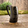 Ladda upp bild i Galleri visare, Et Vikingekrus Valknut Horn (600-800ml), sort og minder om vikingetraditioner, sidder på en træbase på en rustik træoverflade. Hornet er indgraveret med et trekantet design og tre vandrette linjer. I baggrunden er der grønt og en trævæg, der forstærker den naturlige og rustikke stemning.