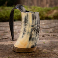 Ladda upp bild i Galleri visare, En Mini Vikingekrus Horn Wave (100 ml) med indviklede keltiske knudeudskæringer og et glat håndtag sidder på en rustik træoverflade. Hornkrusen fremviser en blanding af sorte, hvide og beige nuancer, og dens flade base gør, at den kan stå oprejst.