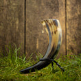 Ladda upp bild i Galleri visare, En poleret Drikkehorn Helleristning med elegante sorte, beige og hvide marmormønstre vises opretstående på et metalstativ. Det rustikke plankeværk og græsbaggrunden skaber naturlige rammer, perfekt til fremvisning på vikingemarked.