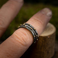 Indlæs billede i Gallery viewer, Nærbillede af en hånd, der viser en stak af tre hamrede 925 Sterling sølv ringe med små gyldne perler, fra Fingerring - Eryn Design - Eni kollektionen. De stabelbare ringe, som bæres på langfingeren, har et elegant dansk design, med en let sløret baggrund, der gør opmærksom på smykkets indviklede detaljer.
