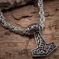 Ladda upp bild i Galleri visare, Et detaljeret nærbillede af et metallisk Mjolnir-vedhæng i form af Thors hammer, med indviklede nordiske designs, fastgjort til en robust og udsmykket flettet Halskæde Kongekæde Stål 6mm. Det vikinge-inspirerede vedhæng og kæde er lavet af rustfrit stål og vist på en robust træoverflade.
