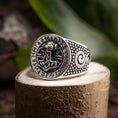 Indlæs billede i Gallery viewer, En Sølvring Thors Hammer 925s Sølv-ring med et detaljeret design hviler på en stenoverflade. Ringens ansigt viser et indviklet mønster med runesymboler, der omkranser et centralt billede af den nordiske hammer, Mjolnir. Siderne har hvirvlende og prikkede designs, mens grønne blade sløres i baggrunden.
