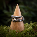 Indlæs billede i Gallery viewer, Fingerringen - Eryn Design - Treasure, en rustik ring fremstillet ved hjælp af Molten Silver-metoden og udsmykket med et tekstureret, naturinspireret design og en lille rund gylden perle, vises på en kegleformet træstativ. Stativet er sat på en bund af mos mod en sløret grøn baggrund, der fremhæver Eryn Designs udsøgte kunstnerskab.
