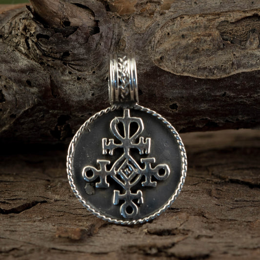 En Rune Amulet Kærlighed Vedhæng 925s Sterling Sølv med et indviklet geometrisk design hænger fra en trægren. Det cirkulære vedhæng er prydet med symmetriske mønstre og symboler, omgivet af en detaljeret, snoet kant. Baggrunden består af groft, struktureret træ.